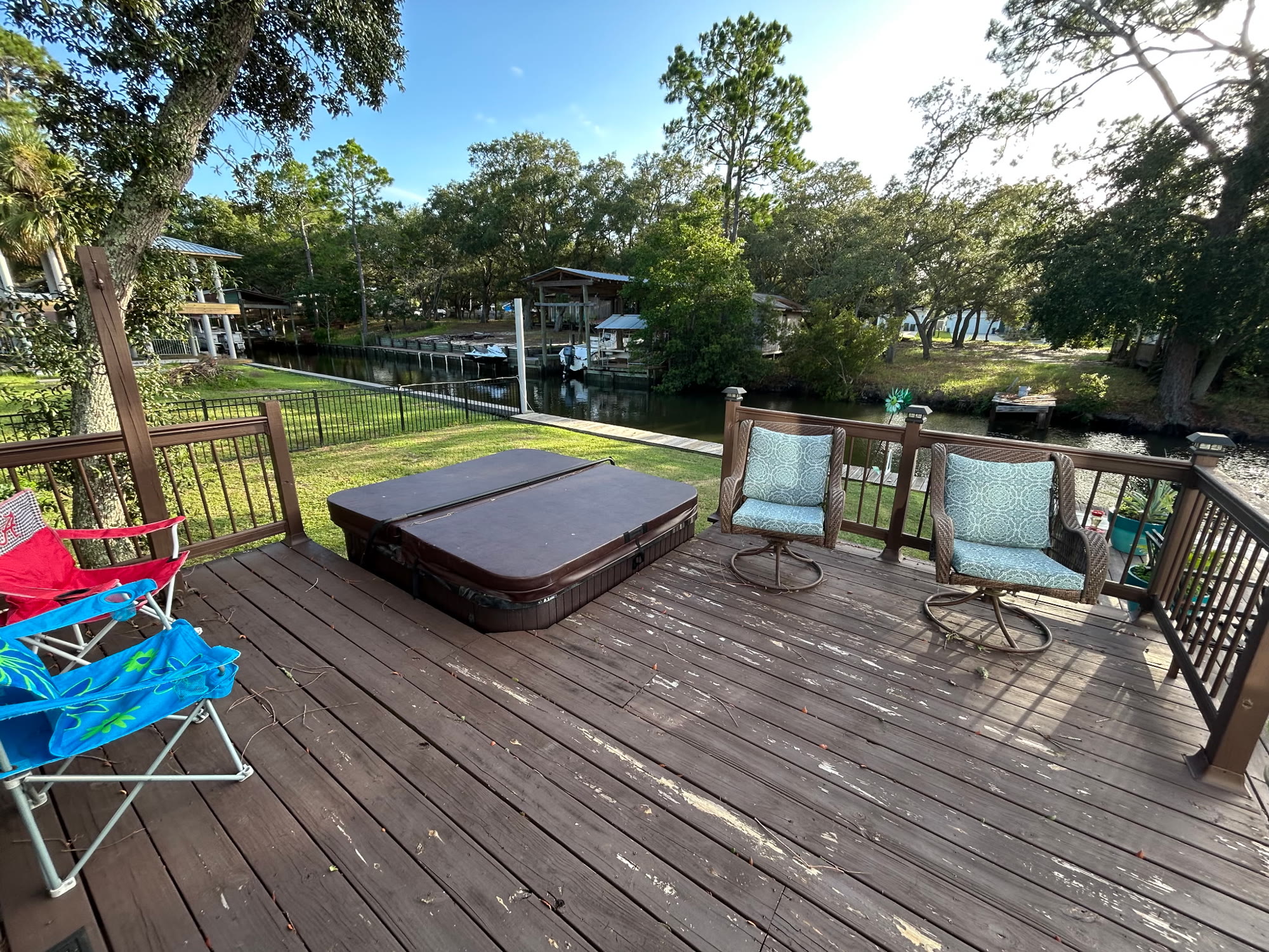 Backyard deck with a hot tub, cushioned swivel chairs, and steps down to the lawn and canal dock