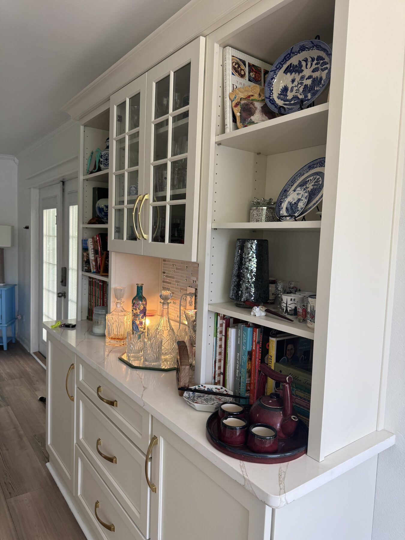 Built-in bar and bookshelf hutch with glass-front cabinets, cookbooks, decanters, and blue-and-white china