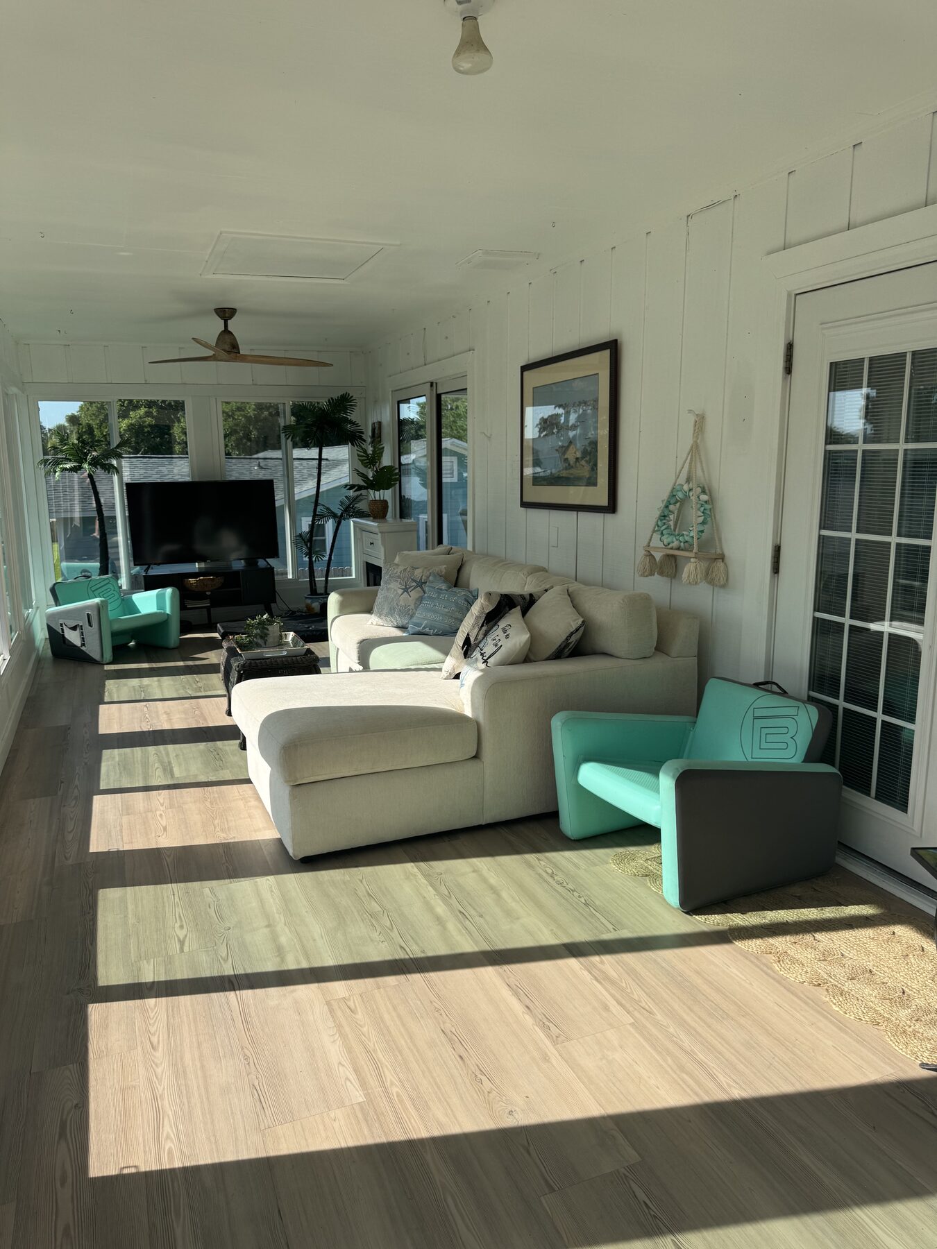 Bright Florida room with a sectional sofa, teal accent chairs, ceiling fan, and windows on three sides