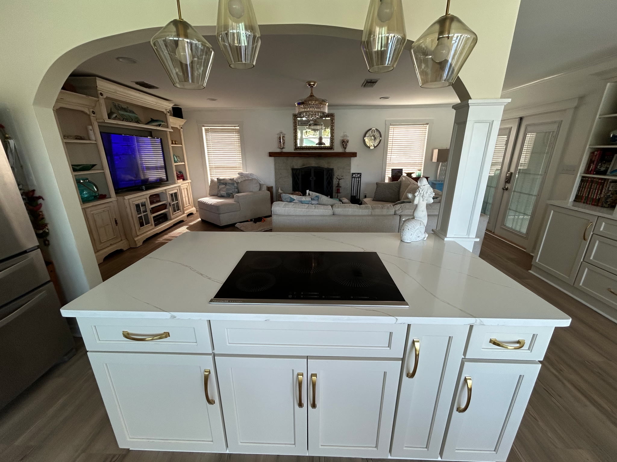 Kitchen island cooktop with pendant lights, opening through an archway to the living room and stone fireplace